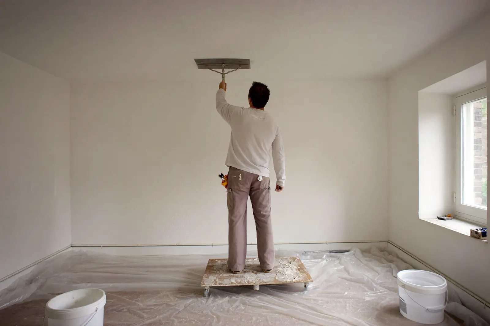 Stukadoor op een rolbordes zet een plafond glad met een brede spaan in een lege kamer