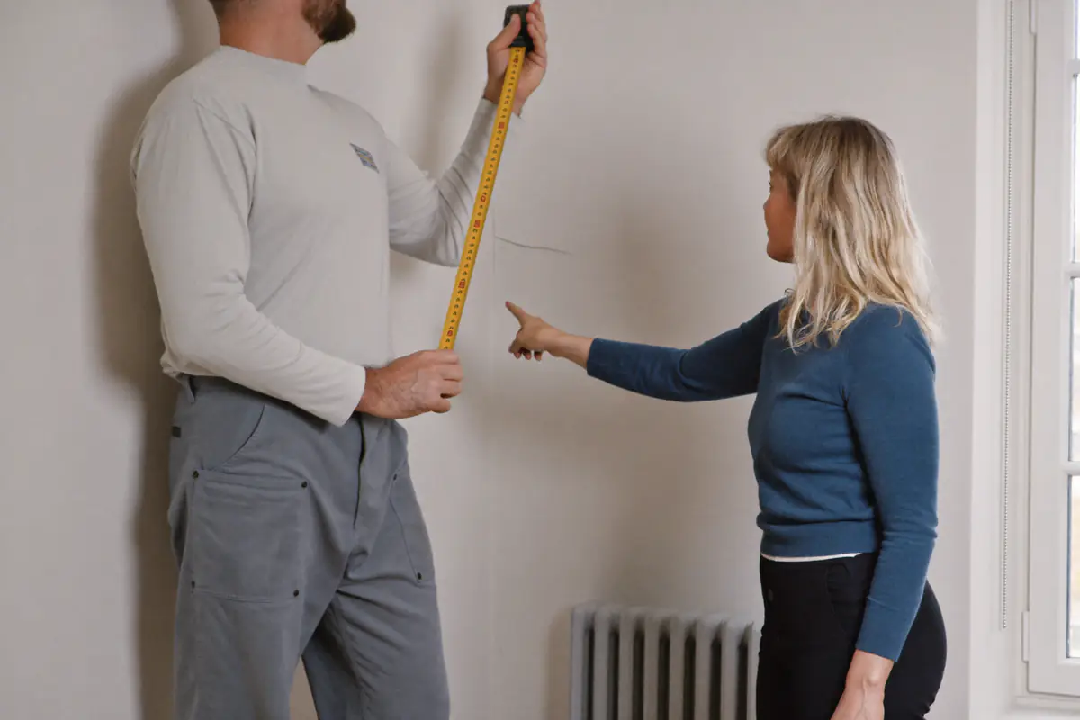 Stukadoor meet een wand op terwijl de bewoner een plek op de muur aanwijst
