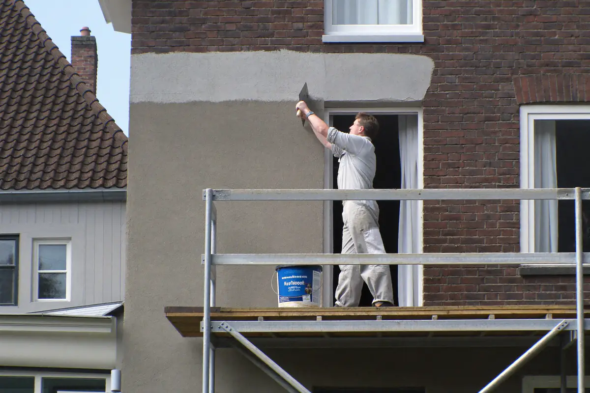 Stukadoor op een steiger zet een grijze pleisterlaag op een bakstenen gevel