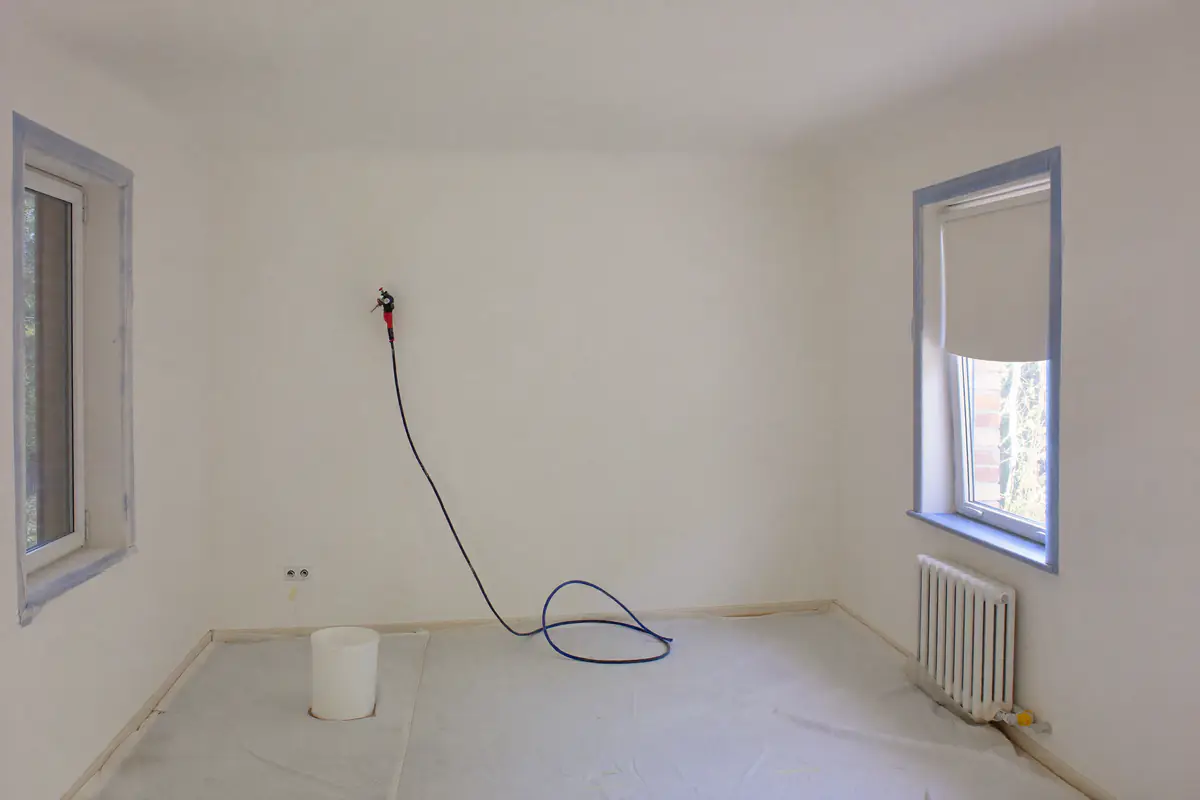 Lege kamer met wit gespoten latex op de wanden en afgeplakte kozijnen