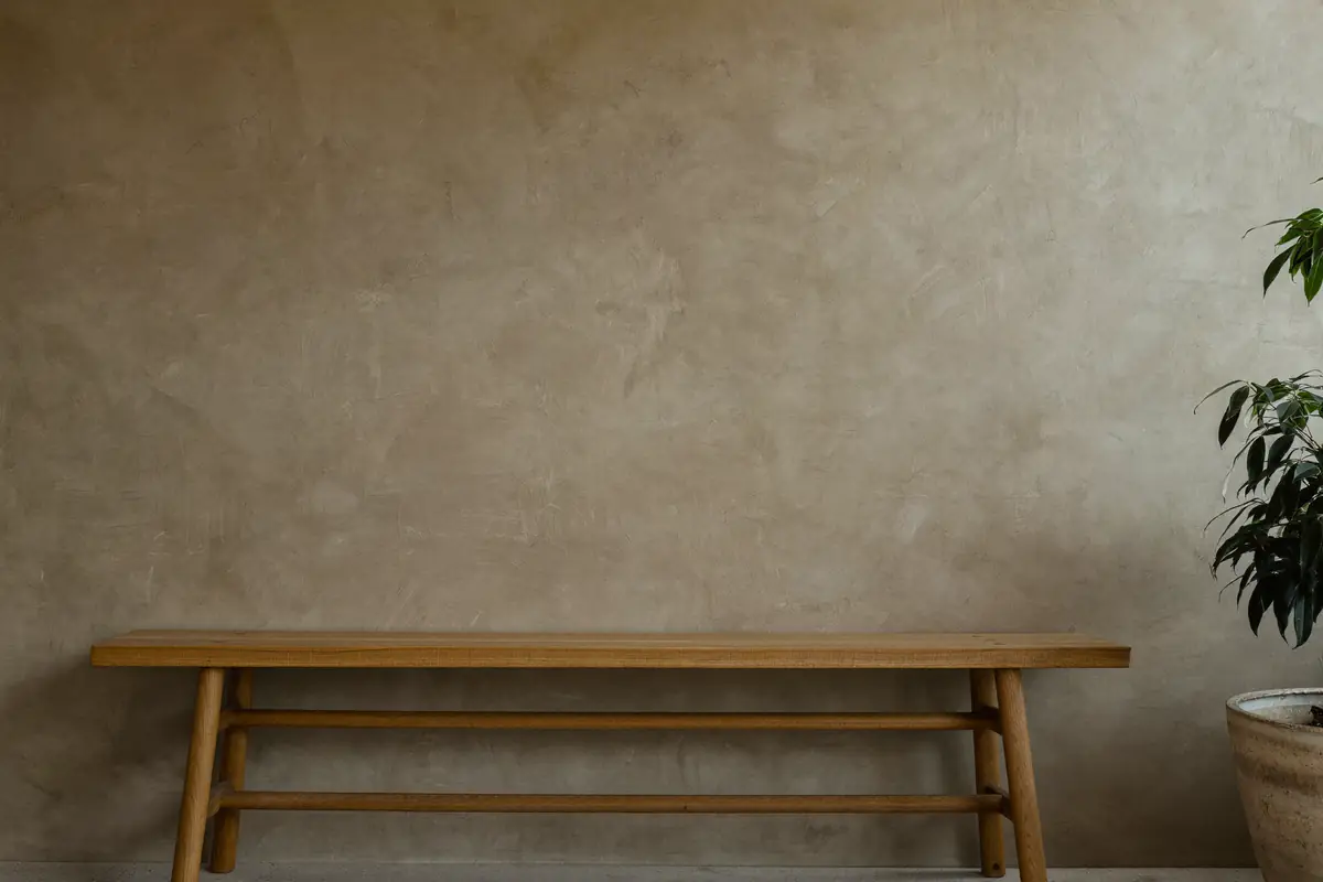 Woonkamerwand met leemstuc in een warme, matte beigetint met een houten bank ervoor