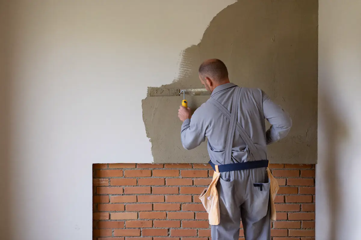 Stukadoor zet gipspleister op een bakstenen binnenmuur, de helft van de wand is al glad