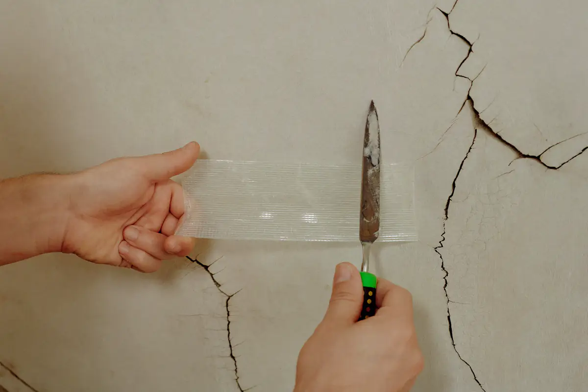 Glasvezelband wordt met een plamuurmes over een scheur in gestuct werk gelegd