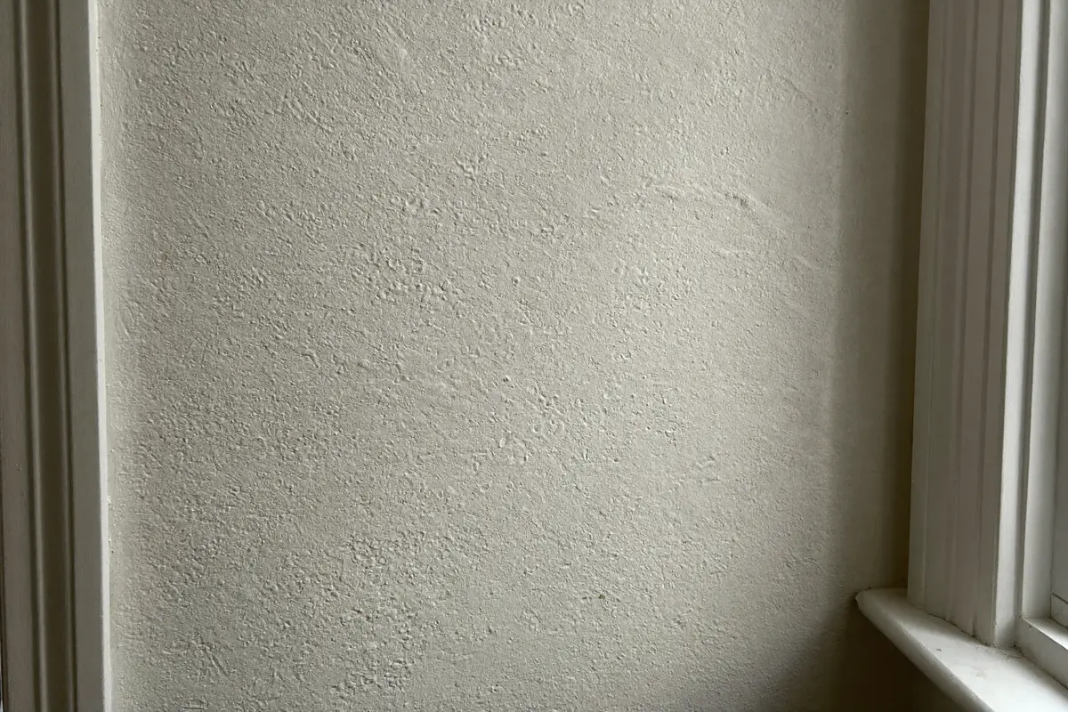 Close-up van een wand met fijne witte sierpleister met een ronde korrel